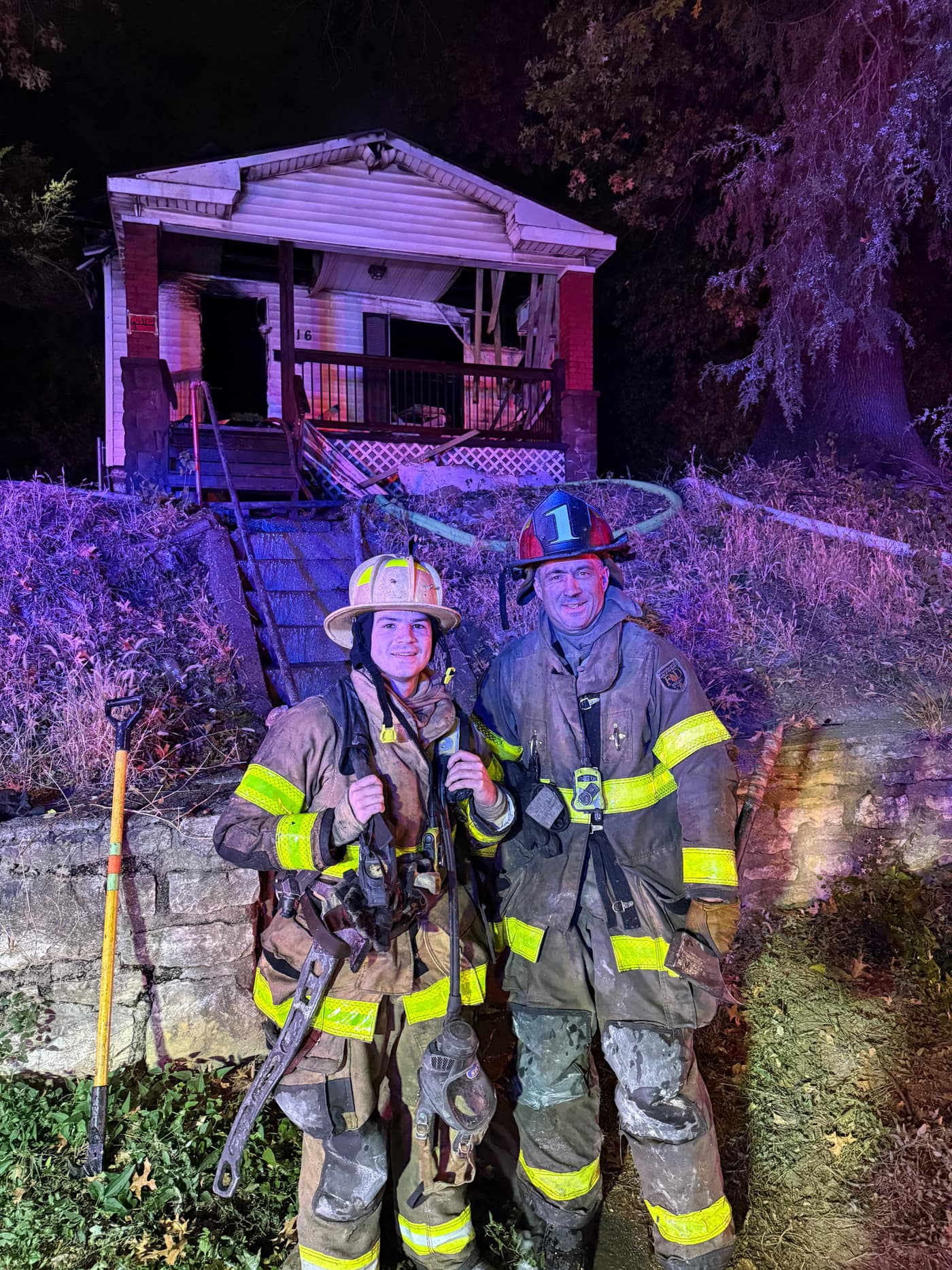 Captain Brian Williams in red captain's helmet and full turnout gear standing with his son at their first working fire together at night