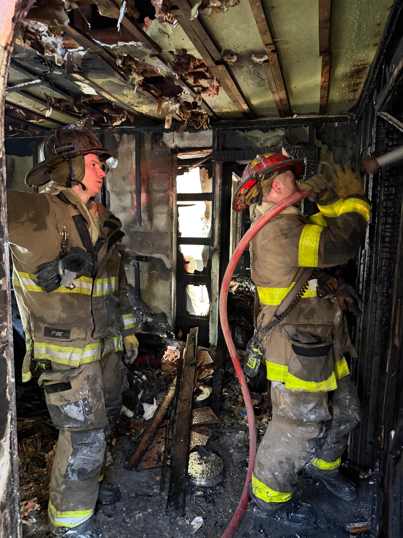 Firefighters working a hose line inside a heavily damaged burned structure on an interior fire attack